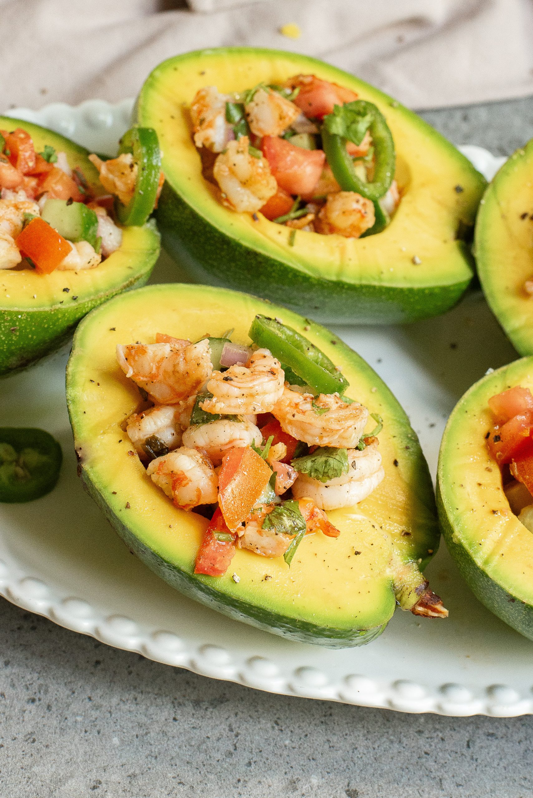 Avocado halves filled with a shrimp and diced vegetable salad, served on a white plate.