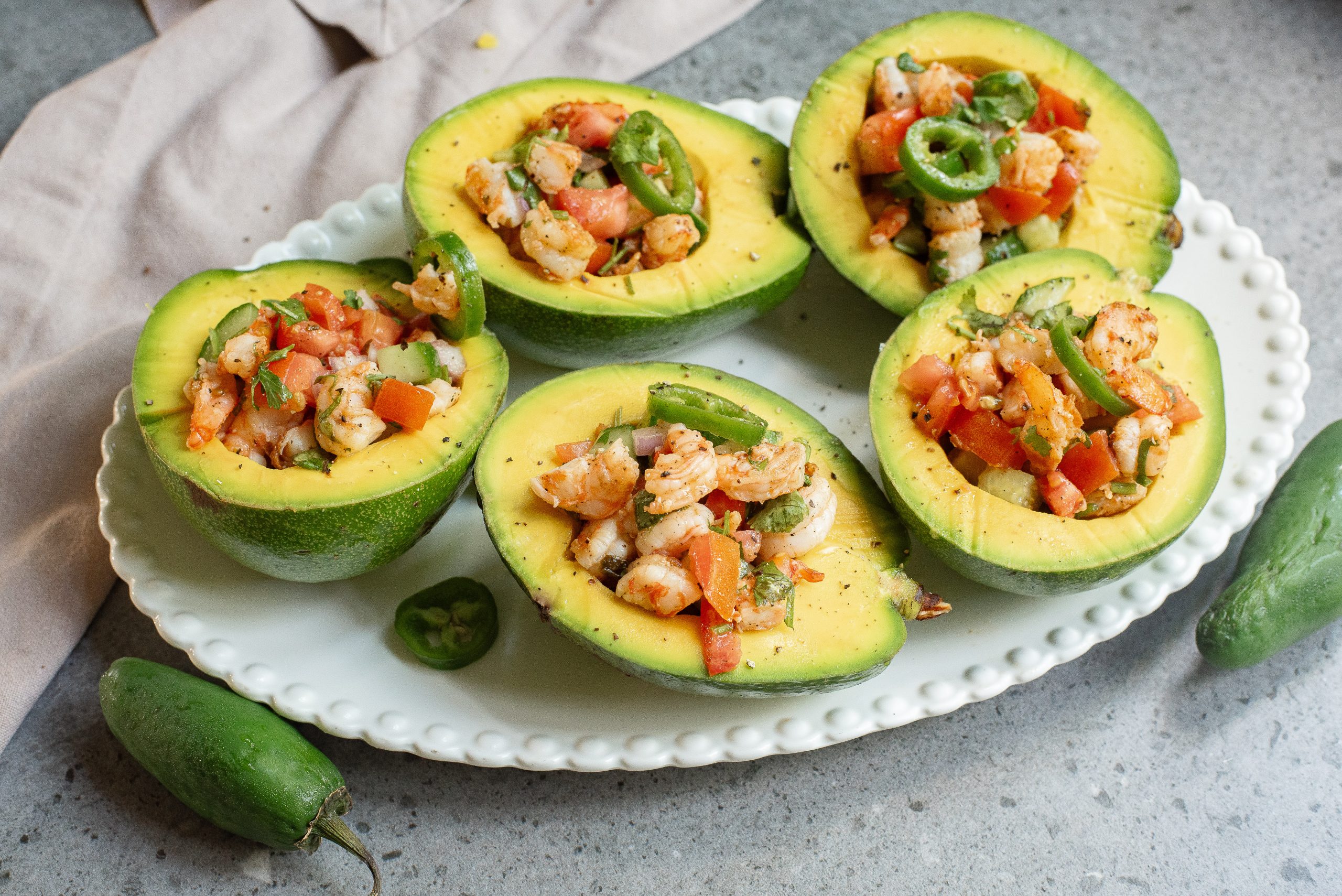 Fresh shrimp ceviche served in halved avocados on a white plate, garnished with cilantro and lime slices.