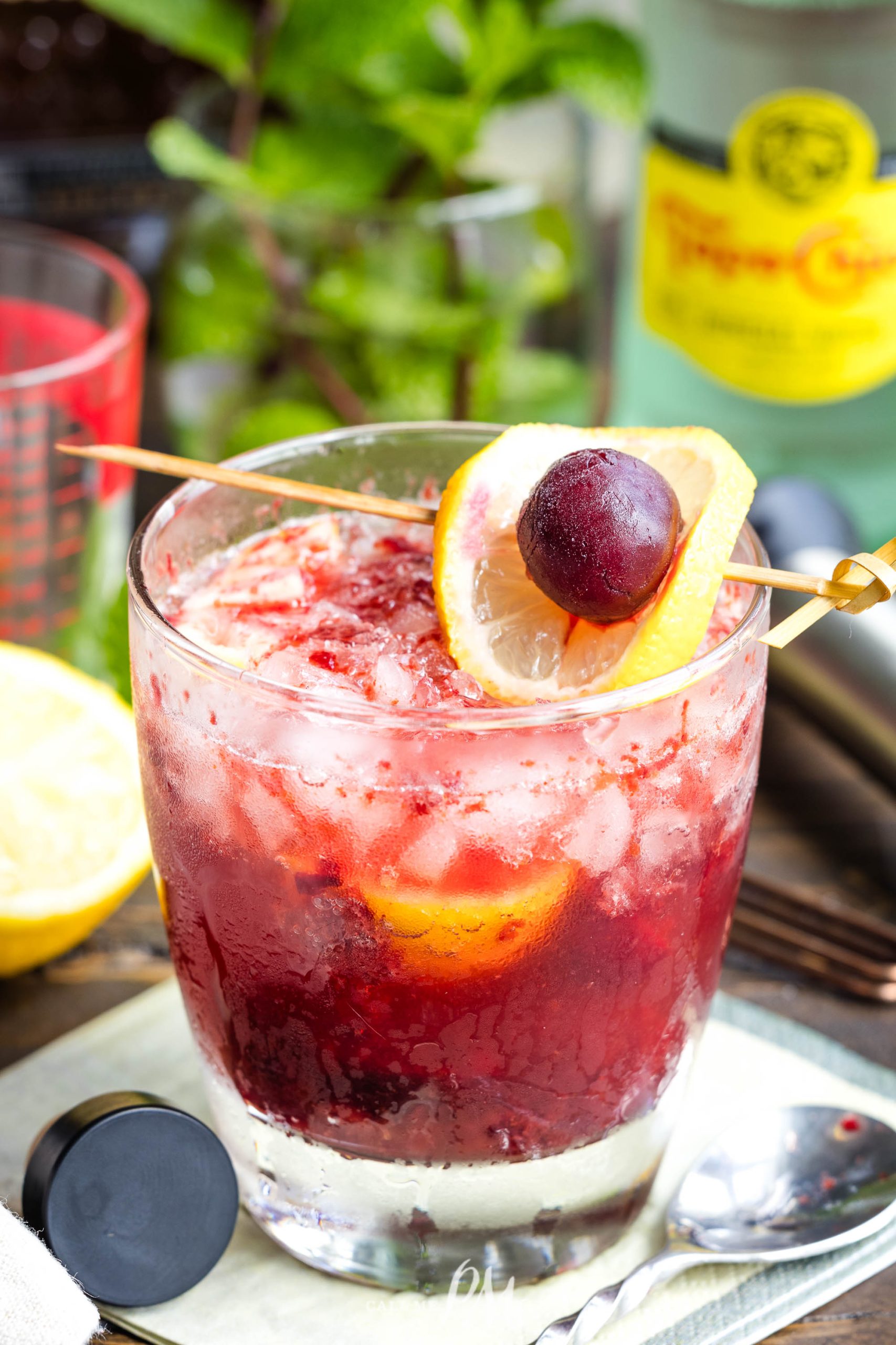 A Fizzy Cherry Bourbon Sour cocktail with crushed ice, adorned with a cherry and lemon slice, served in a glass on a rustic table with a vibrant background.