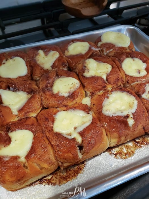 Freshly baked cinnamon rolls with cream cheese frosting on a baking sheet.