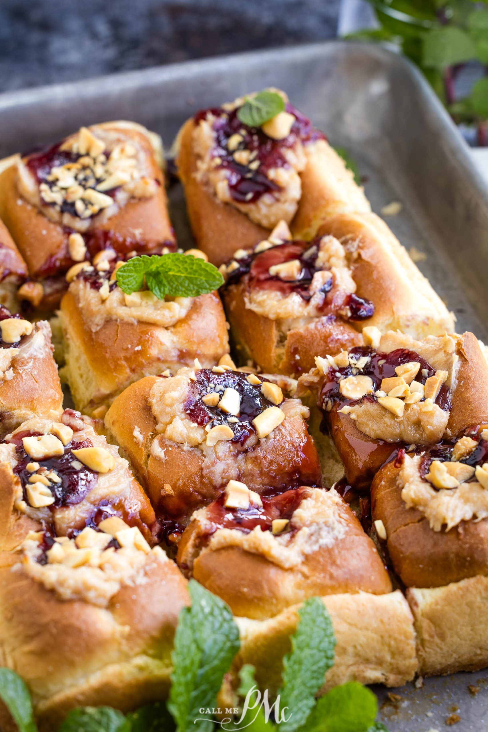 A tray of freshly baked sweet rolls topped with nuts and a fruit glaze, garnished with mint leaves.