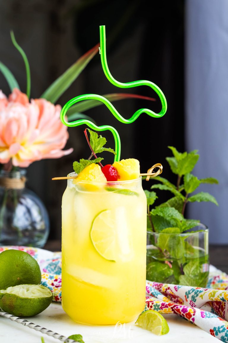 A glass of yellow liquid with fruit on top.