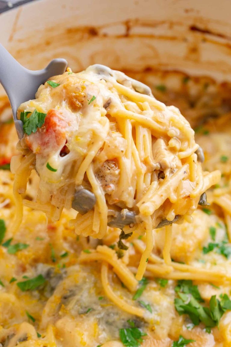 A ladle scoops a portion of cheesy baked spaghetti with tomatoes and herbs from a pot.