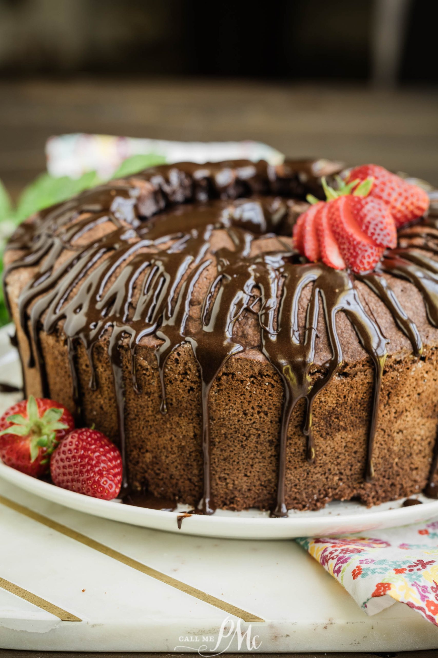 A chocolate cake on a white plate, drizzled with chocolate sauce and garnished with fresh strawberries.