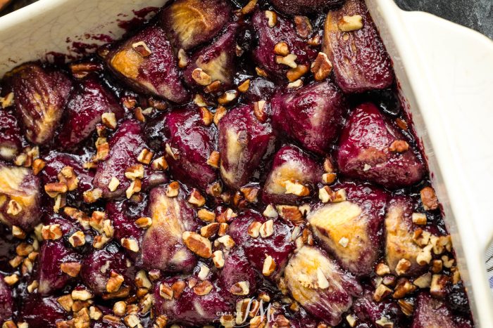 A close-up photo of a baked dish filled with caramelized figs and sprinkled with chopped nuts in a white rectangular baking dish.
