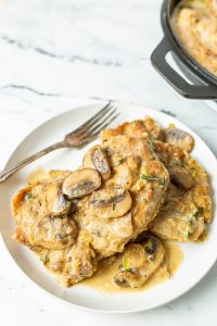 A plated dish of creamy chicken topped with sliced mushrooms, served on a white plate with a fork.
