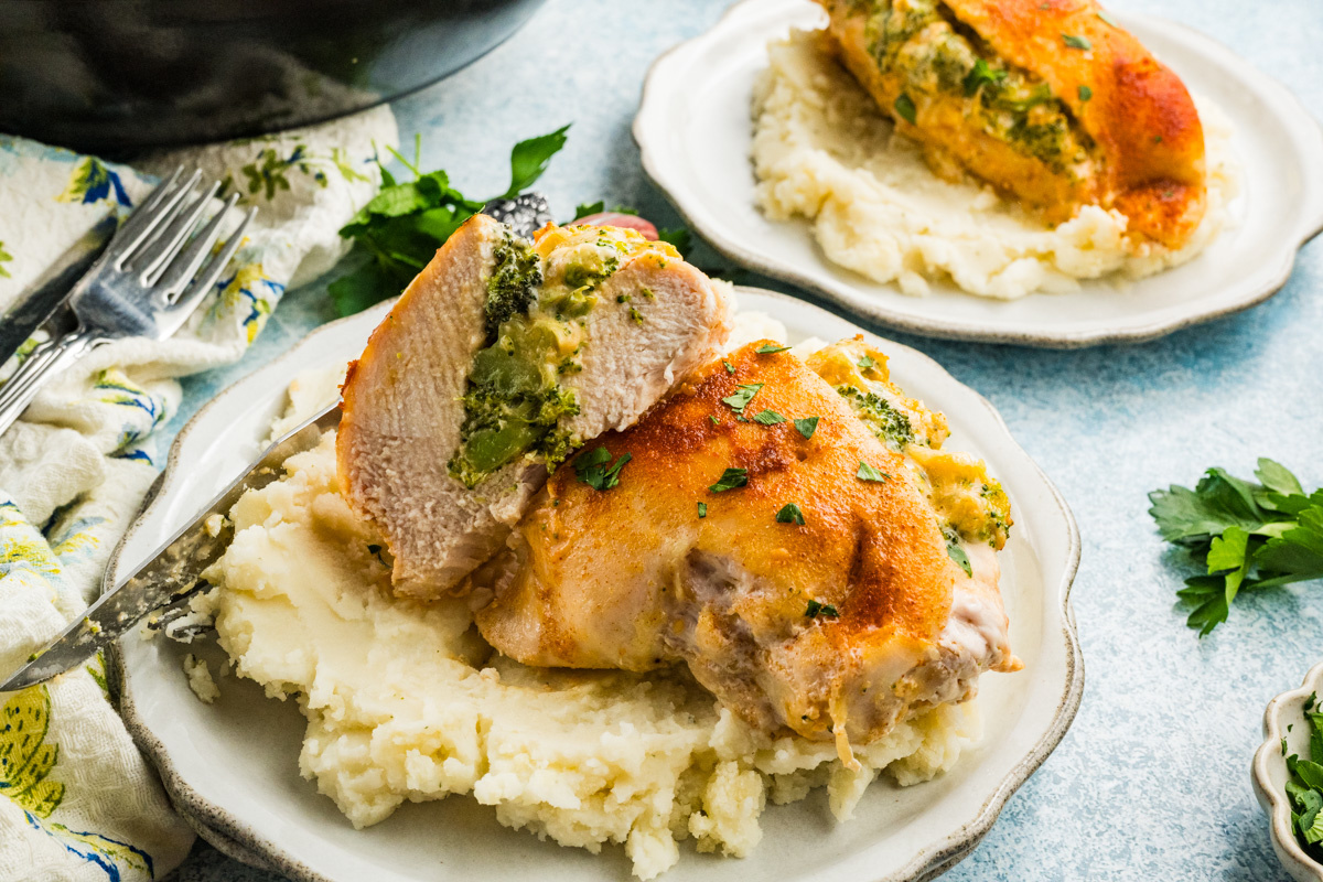 Broccoli stuffed buffalo chicken breasts with cheese, served on mashed potatoes and garnished with chopped herbs, presented on a ceramic plate.