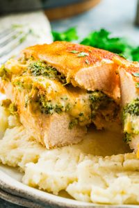 Broccoli stuffed buffalo chicken breasts, sliced and filled with cheese, are served on a bed of creamy mashed potatoes.