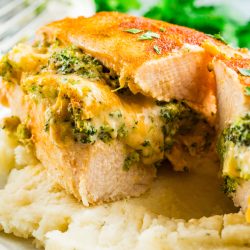 Broccoli stuffed buffalo chicken breasts, sliced and filled with cheese, are served on a bed of creamy mashed potatoes.