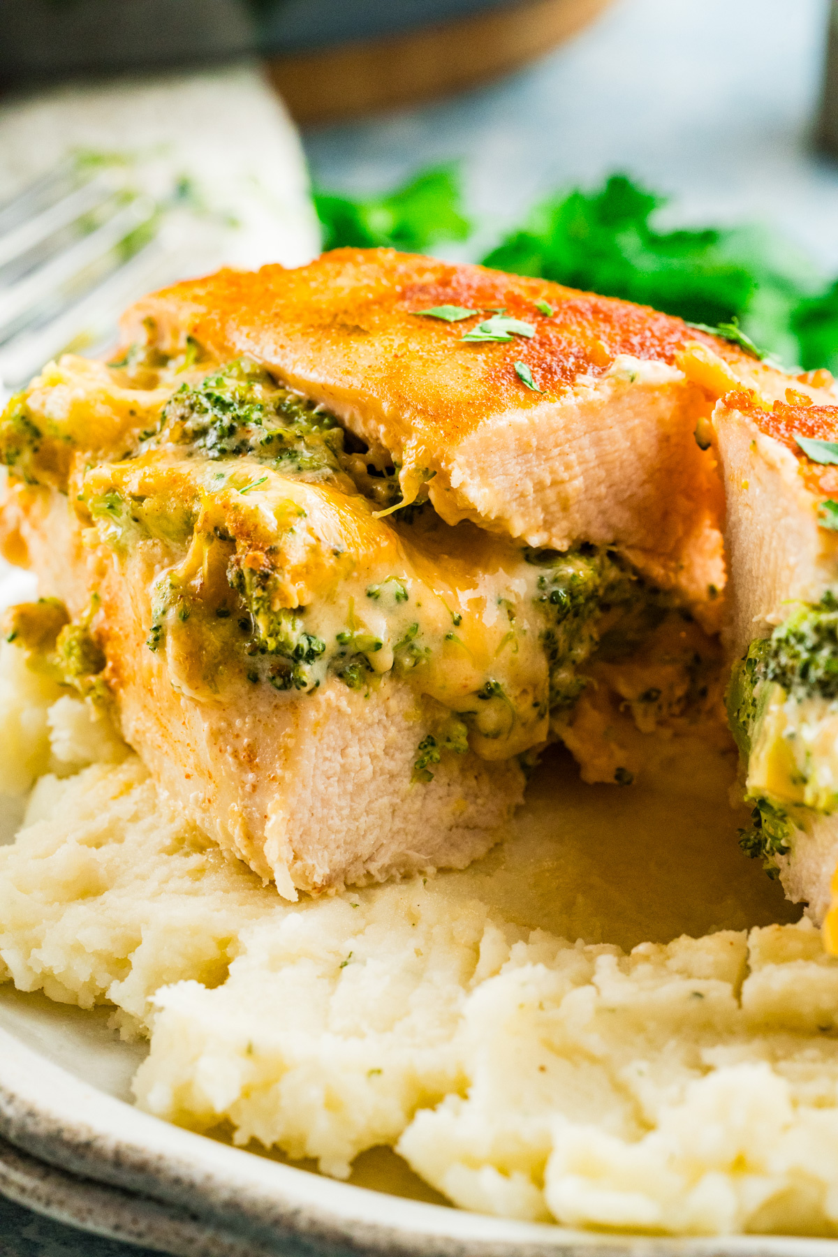 Broccoli stuffed buffalo chicken breasts, sliced and filled with cheese, are served on a bed of creamy mashed potatoes.