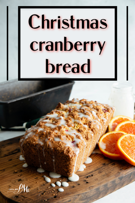 Loaf of Christmas cranberry bread with icing on a wooden board, garnished with orange slices, next to a baking tin, showcasing the delicious Christmas Cranberry Bread Recipe.