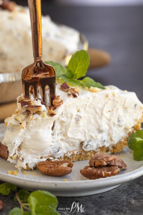 Cook in June. A fork slices into a creamy pie topped with chopped pecans, displayed on a plate with whole pecans and mint leaves.