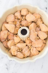 Unbaked monkey bread pieces coated in cinnamon sugar and sprinkled with walnuts, arranged in a Bundt pan.