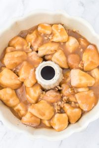 A bundt pan filled with unbaked monkey bread dough, coated in brown sugar glaze and sprinkled with nuts, on a marble surface.