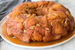 Plate of sticky monkey bread with caramel sauce and walnuts on a marble surface.