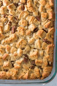 Close-up of a glass baking dish filled with bread pudding featuring chunks of bread and visible pecans, with a golden-brown crust.