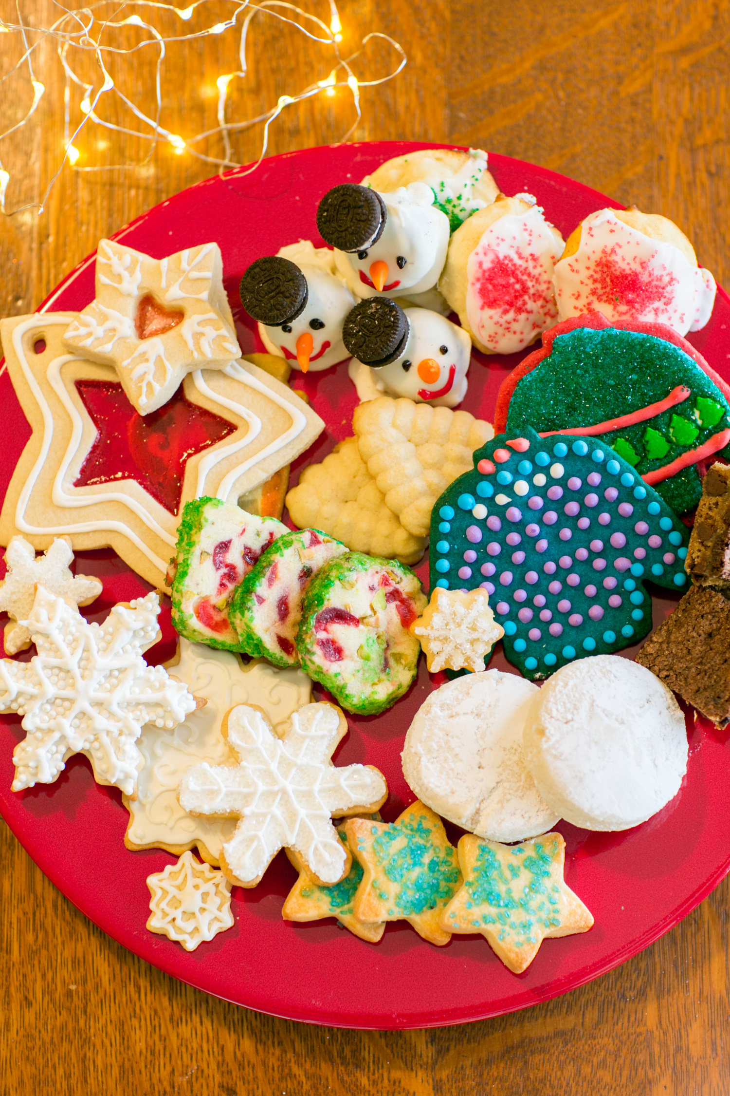 A festive cookie roundup features a variety of decorated Christmas cookies on a red plate, including snowflakes, stars, and colorful frosted designs. Perfect for any cookie swap, these treats add a delightful charm to your holiday celebrations.