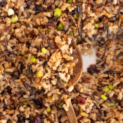 A bowl of mixed wild rice with chopped green onions and cranberries, stirred with a wooden spoon.