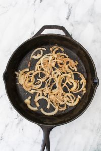 Sliced onions cooking in a black cast iron skillet on a white marble surface.