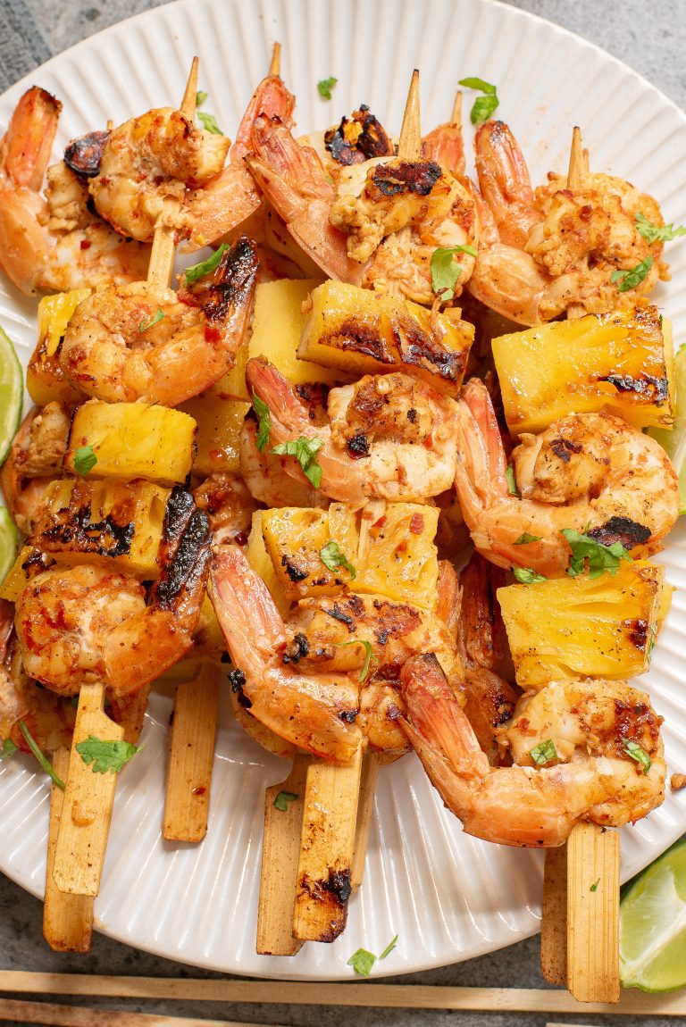 Grilled shrimp and pineapple skewers garnished with cilantro on a white plate.