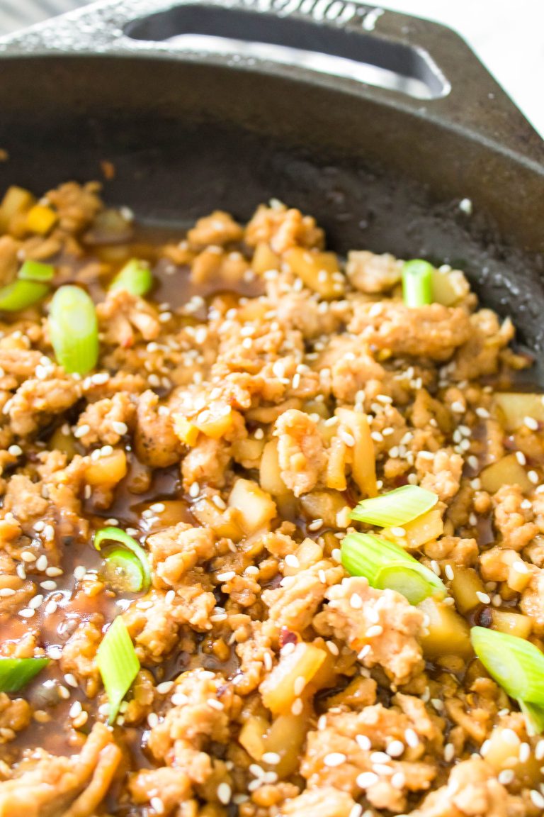 A pan of seasoned ground meat with diced vegetables, topped with sesame seeds and chopped green onions.