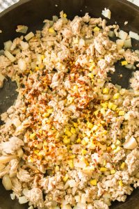 General Tso's Ground Chicken sizzles in a pan with chopped onions, minced garlic, and red pepper flakes, creating a savory aroma.