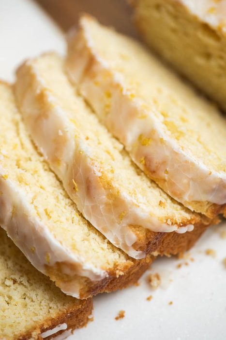 Sliced lemon loaf cake with a glaze frosting on a white surface.