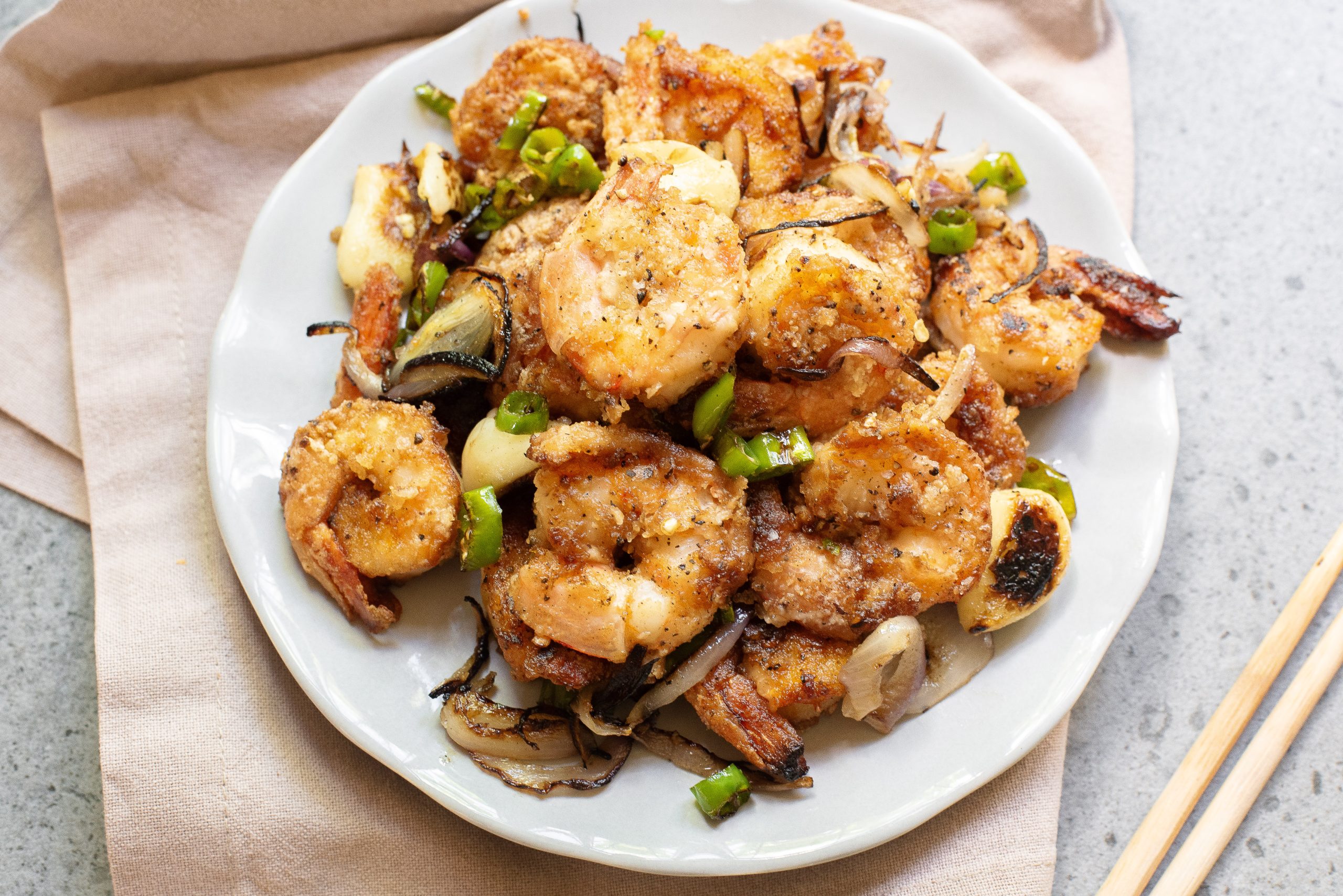 A white plate with seafood, sliced onions, and chopped green peppers on a beige napkin.