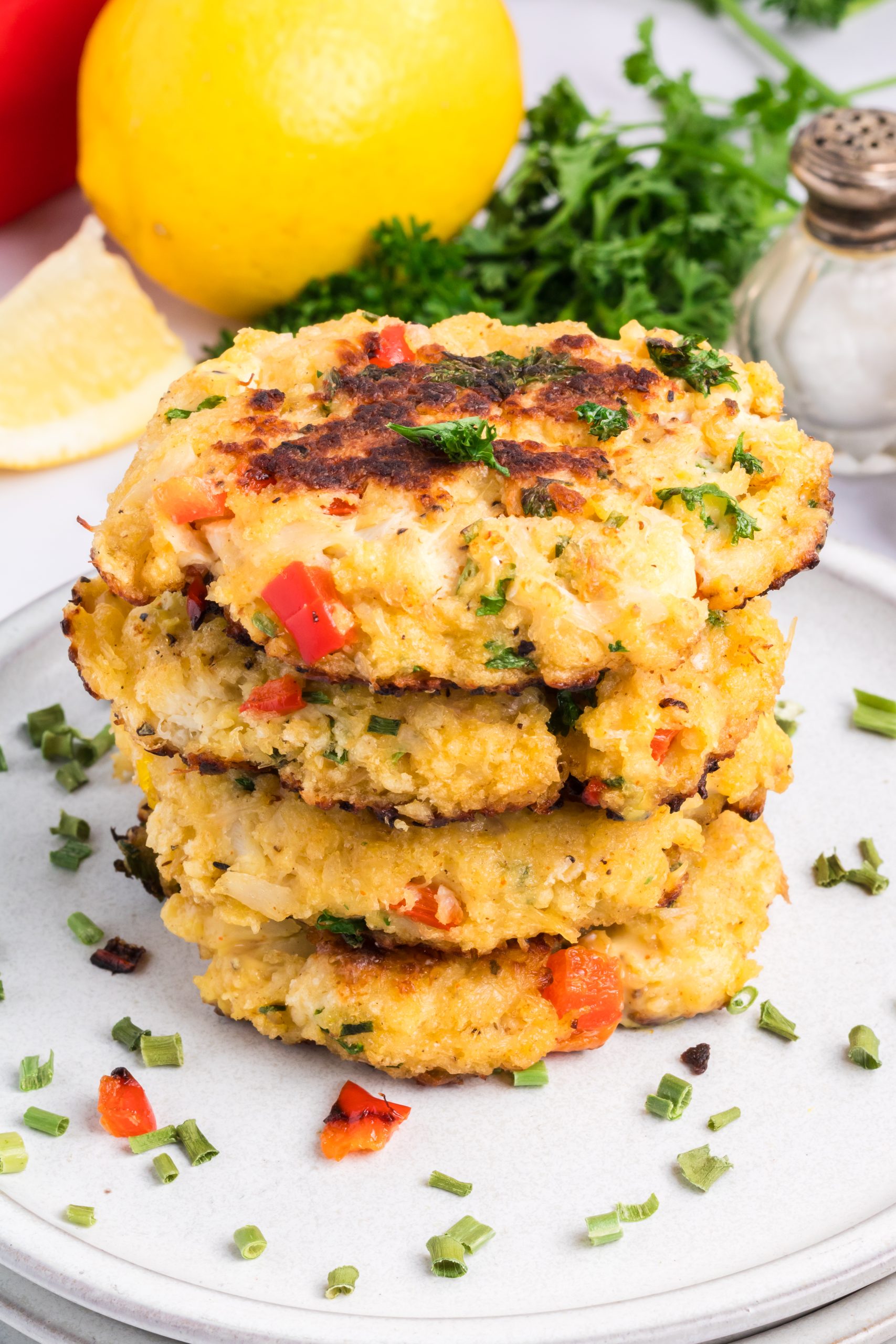 A stack of four Classic Crab Cakes with visible red peppers and herbs on a white plate, garnished with chopped chives.