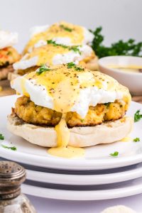 An English muffin topped with a crab cake, poached egg, and hollandaise sauce, garnished with parsley, on a white plate.