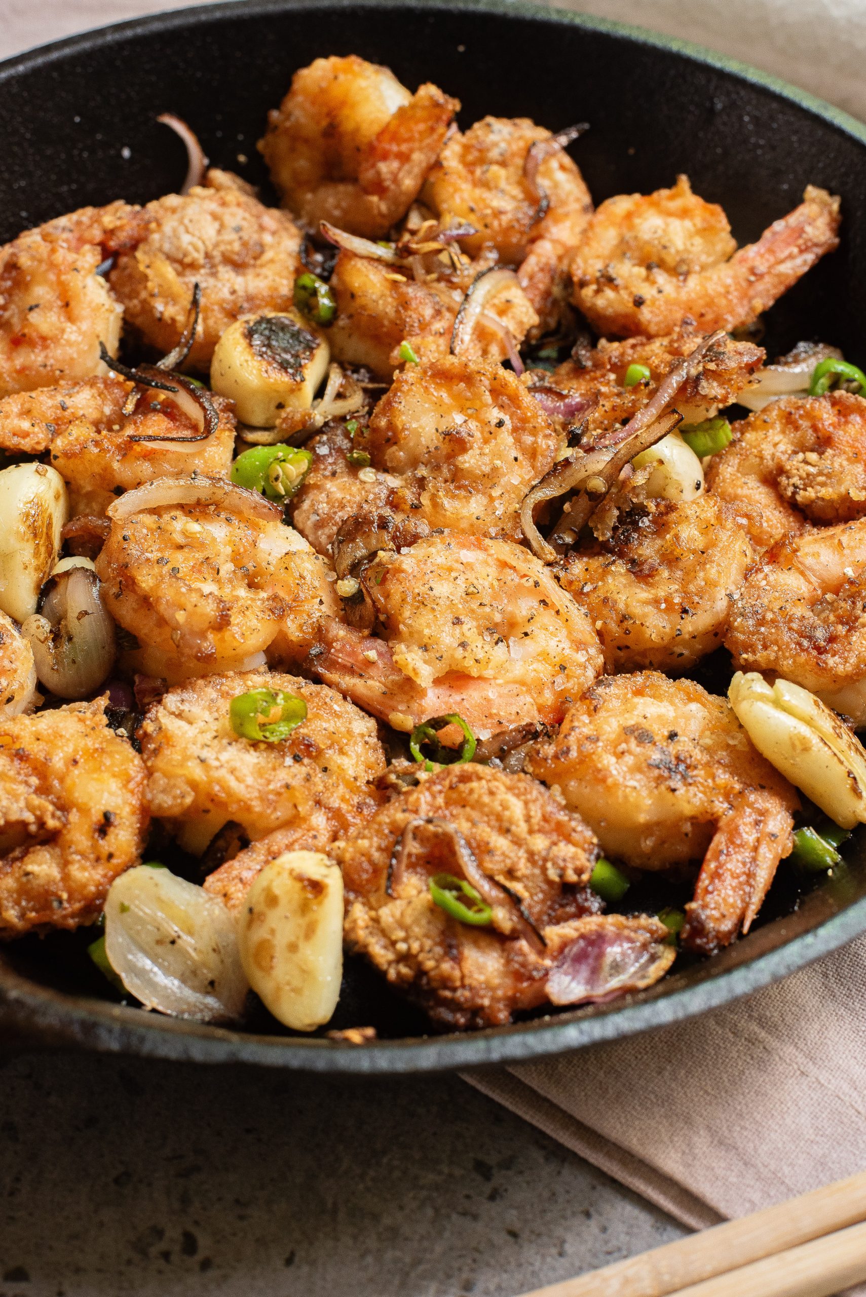 A skillet filled with seasoned, cooked shrimp, sliced garlic, and green chili peppers, garnished with cracked black pepper.