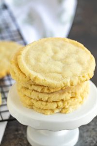 A stack of sugar cookies on a white pedestal, with a wire cooling rack in the background.