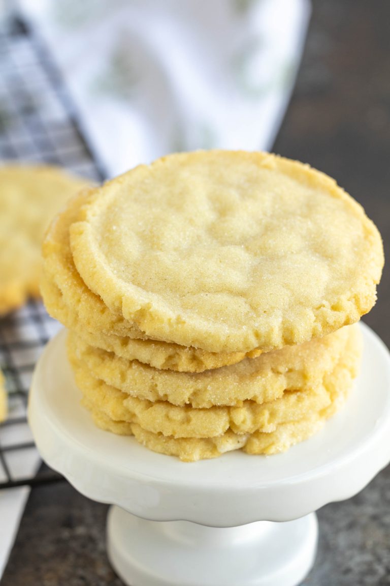 A stack of sugar cookies on a white pedestal, with a wire cooling rack in the background.
