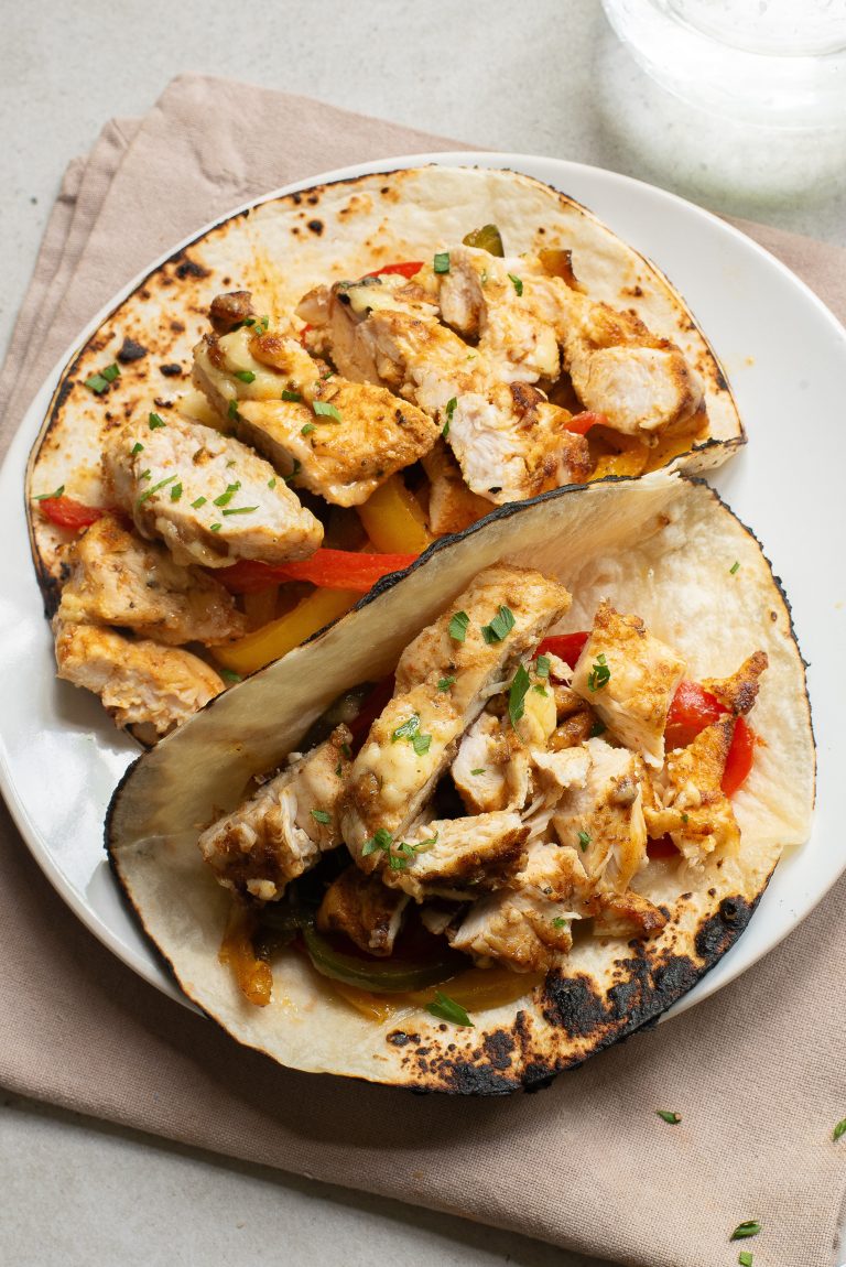 Two grilled chicken fajita tacos with sliced chicken, bell peppers, and herbs on toasted tortillas, served on a white plate.