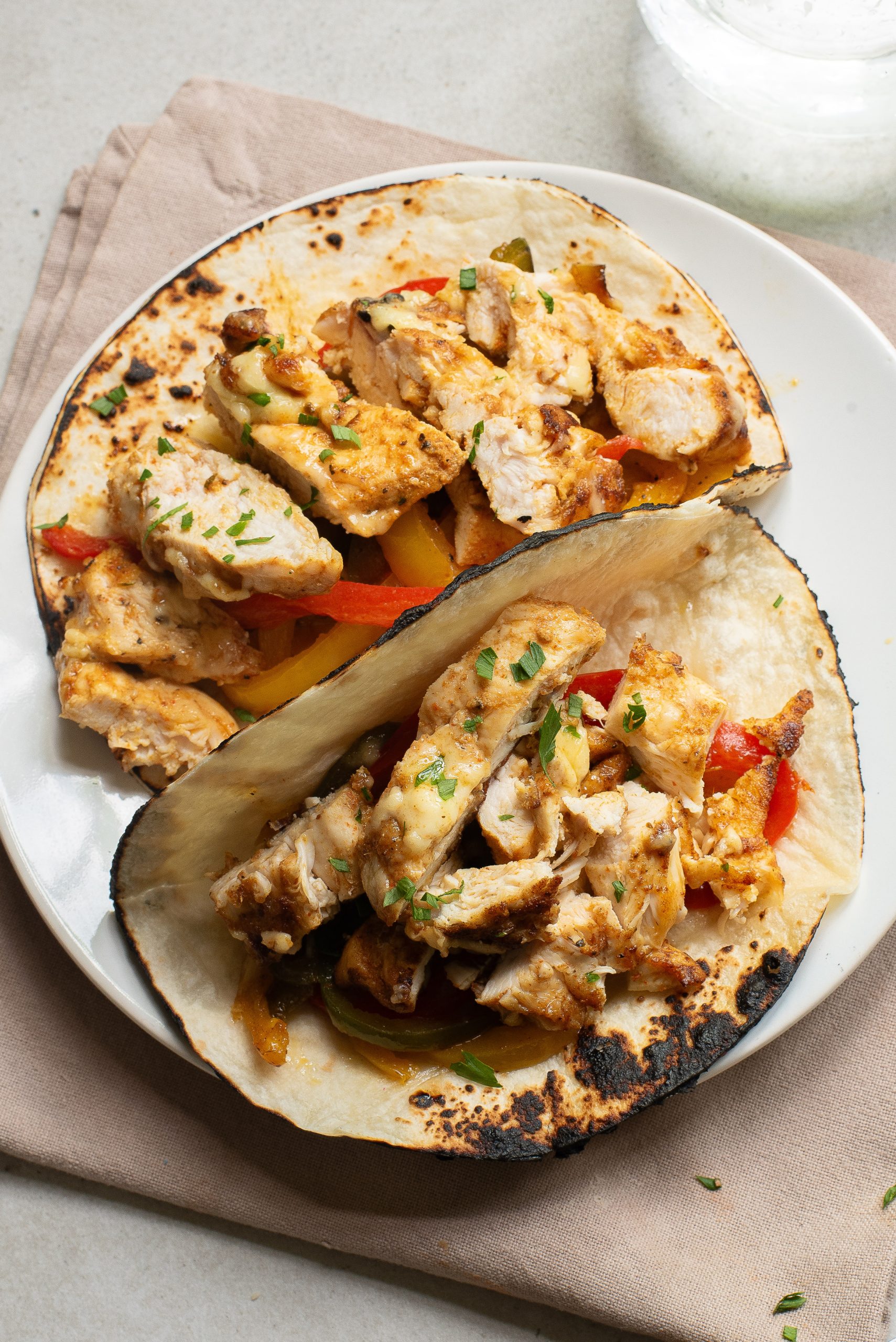 Two grilled Stovetop Chicken Tacos with sliced chicken, bell peppers, and herbs on toasted tortillas, served on a white plate.