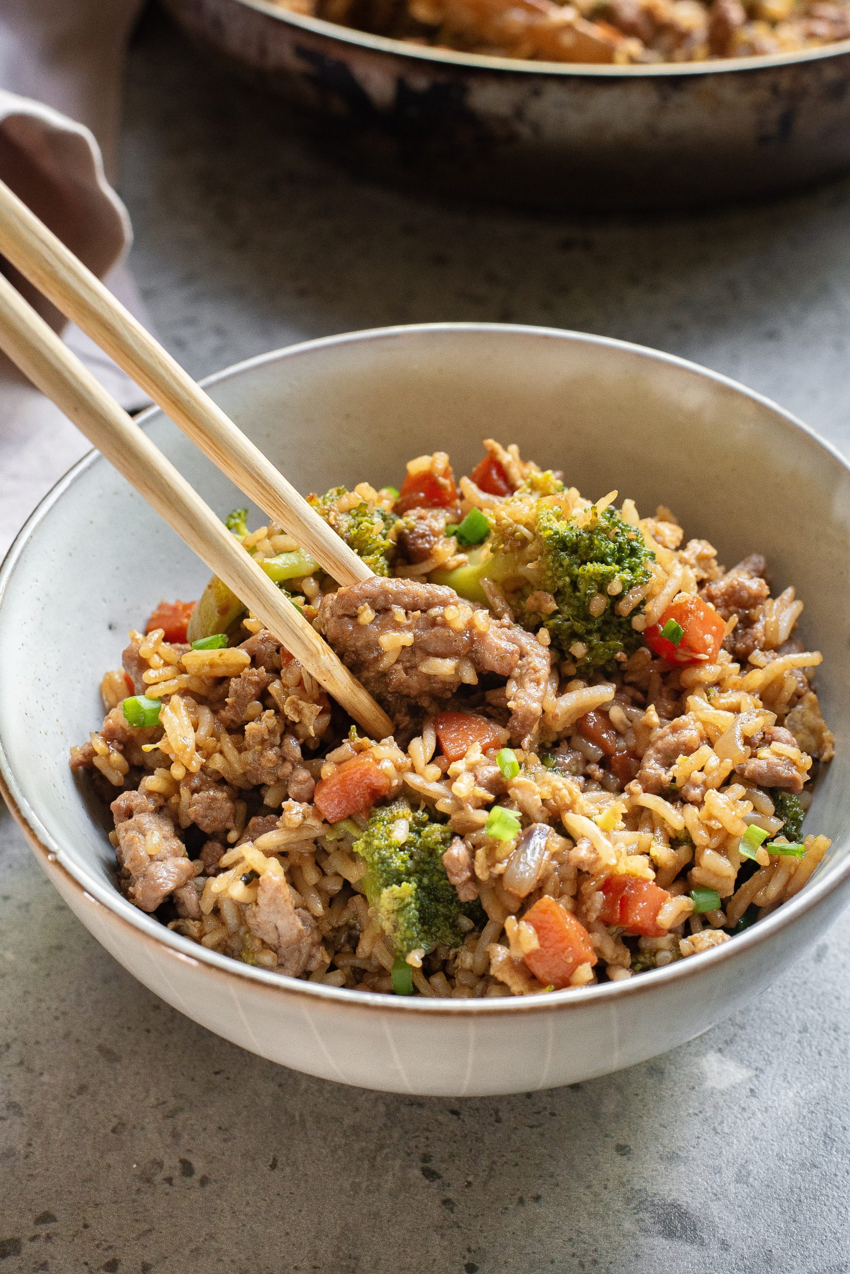 A bowl of food is being picked up with chopsticks.