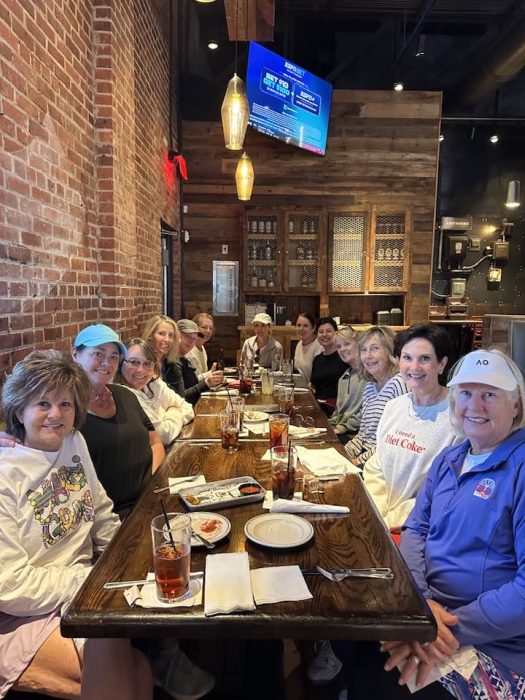 A group of people sitting together at a long wooden table in a restaurant, enjoying drinks and empty plates in front of themโan evening that could easily make Paula's Picks for memorable gatherings.
