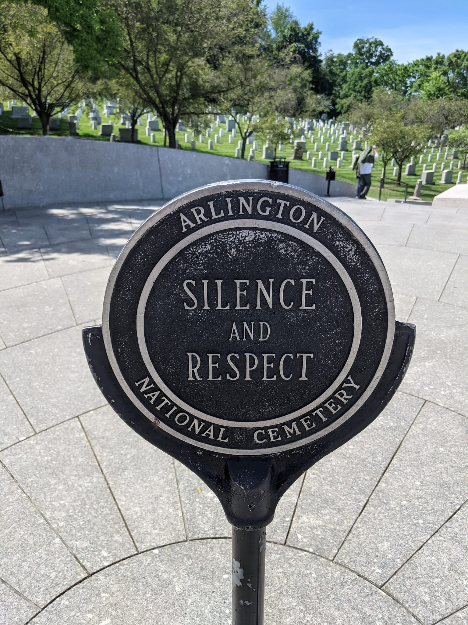 A sign at Arlington National Cemetery reads "Silence and Respect," with rows of headstones and trees visible in the background.