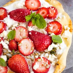 Flatbread topped with whipped cheese, whole and sliced strawberries, crumbled feta, sunflower seeds, and fresh mint leaves.