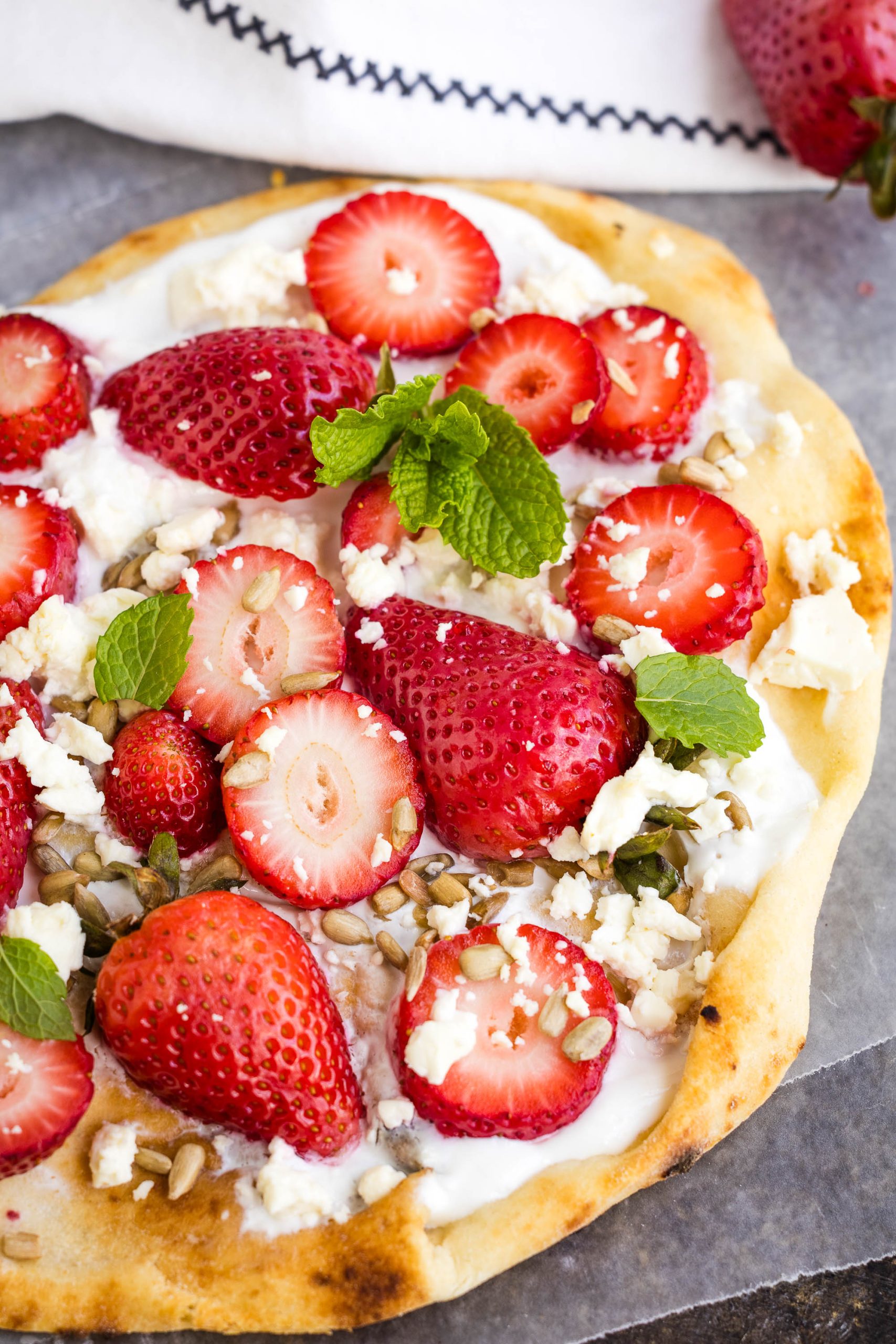 Flatbread topped with whipped cheese, whole and sliced strawberries, crumbled feta, sunflower seeds, and fresh mint leaves.