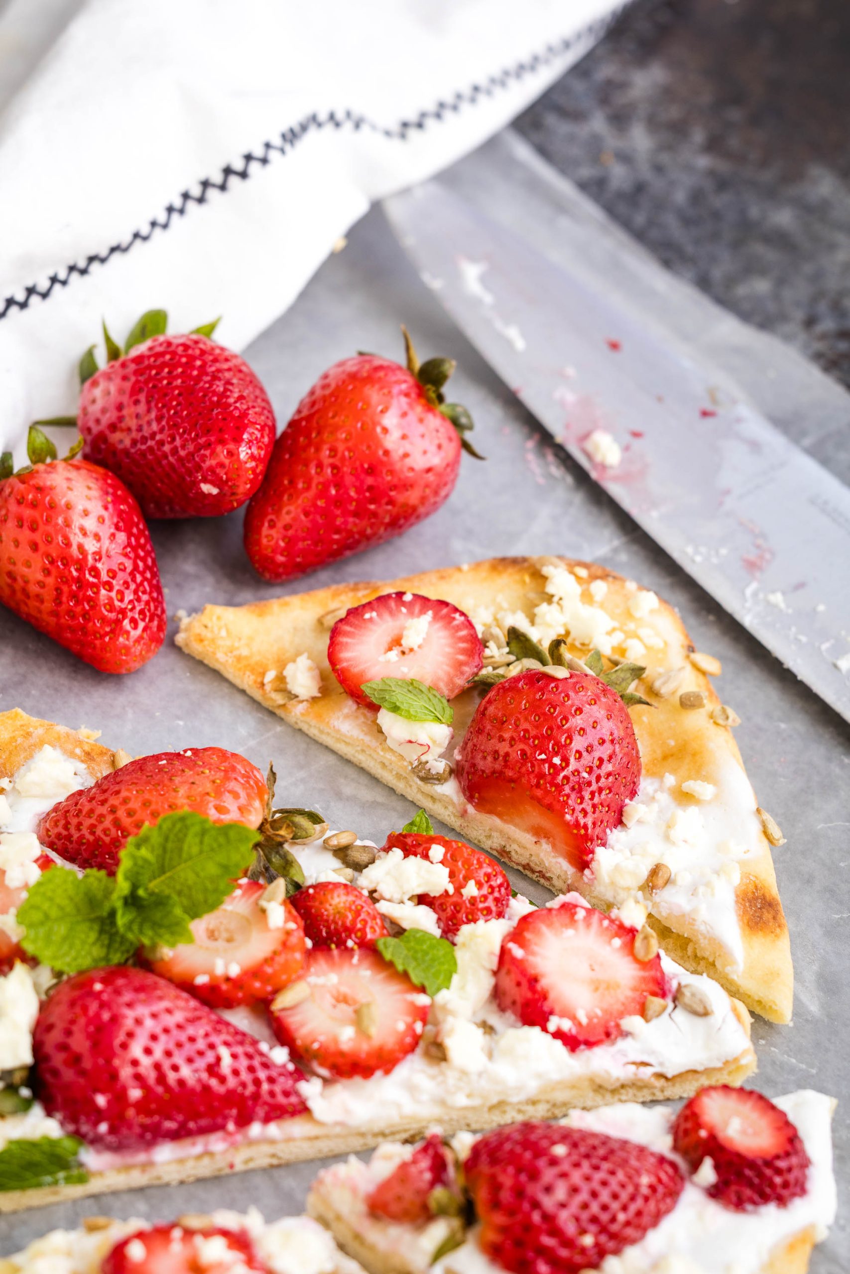 Sliced nana topped with fruit and a large knife on a parchment-lined surface.