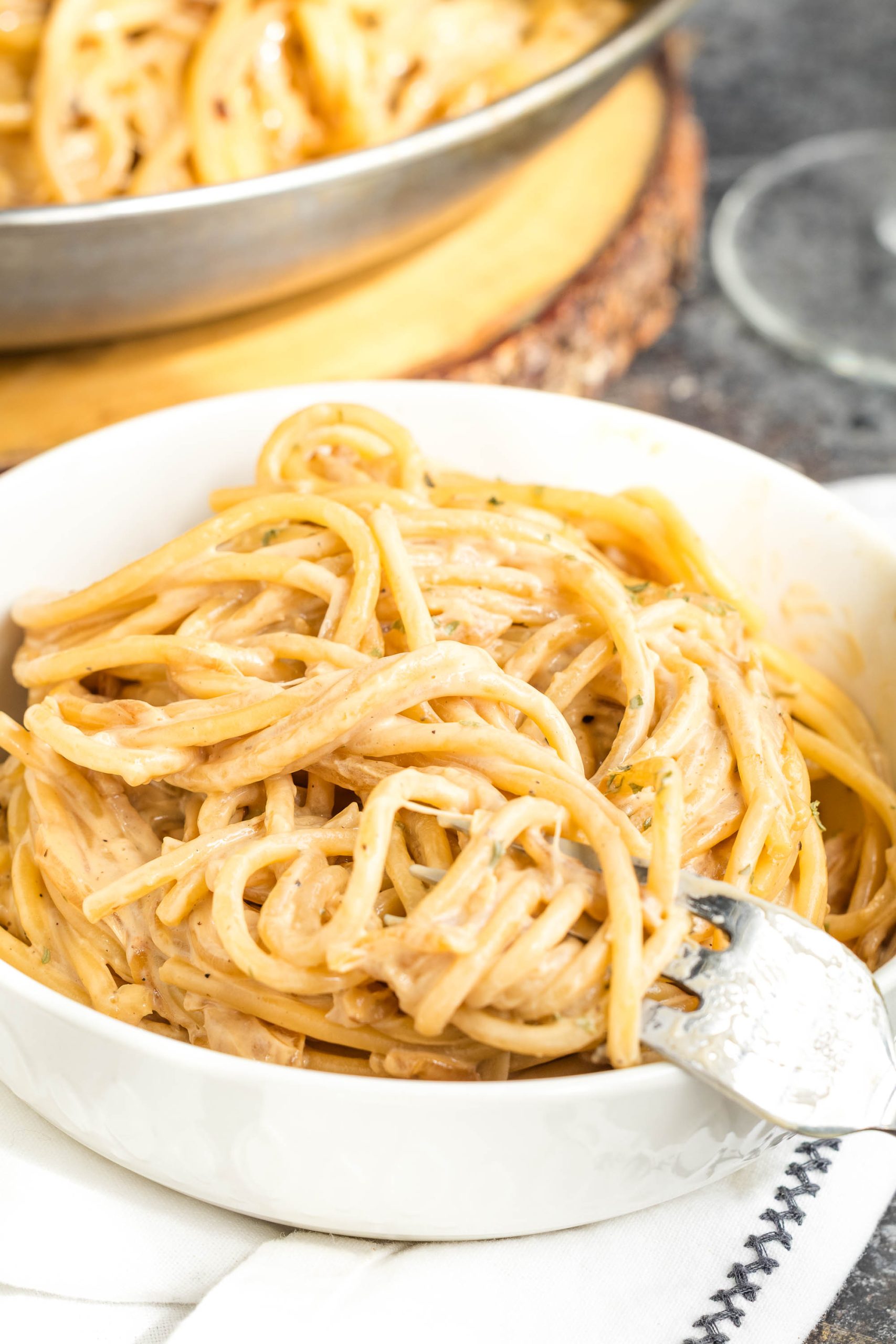A white bowl filled with noodles, with a fork twirling some noodles; another dish of pasta is visible in the background.