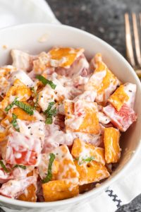 A bowl of creamy salad with Cheez-It crackers, tomato pieces, fresh herbs, and a mayonnaise-based dressing.