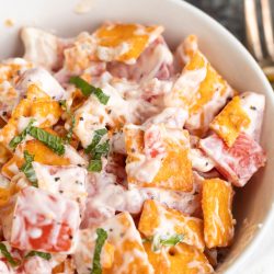 A bowl of creamy salad with Cheez-It crackers, tomato pieces, fresh herbs, and a mayonnaise-based dressing.