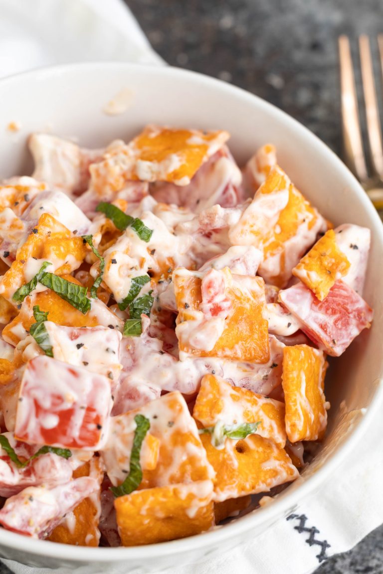 A bowl of creamy salad with Cheez-It crackers, tomato pieces, fresh herbs, and a mayonnaise-based dressing.