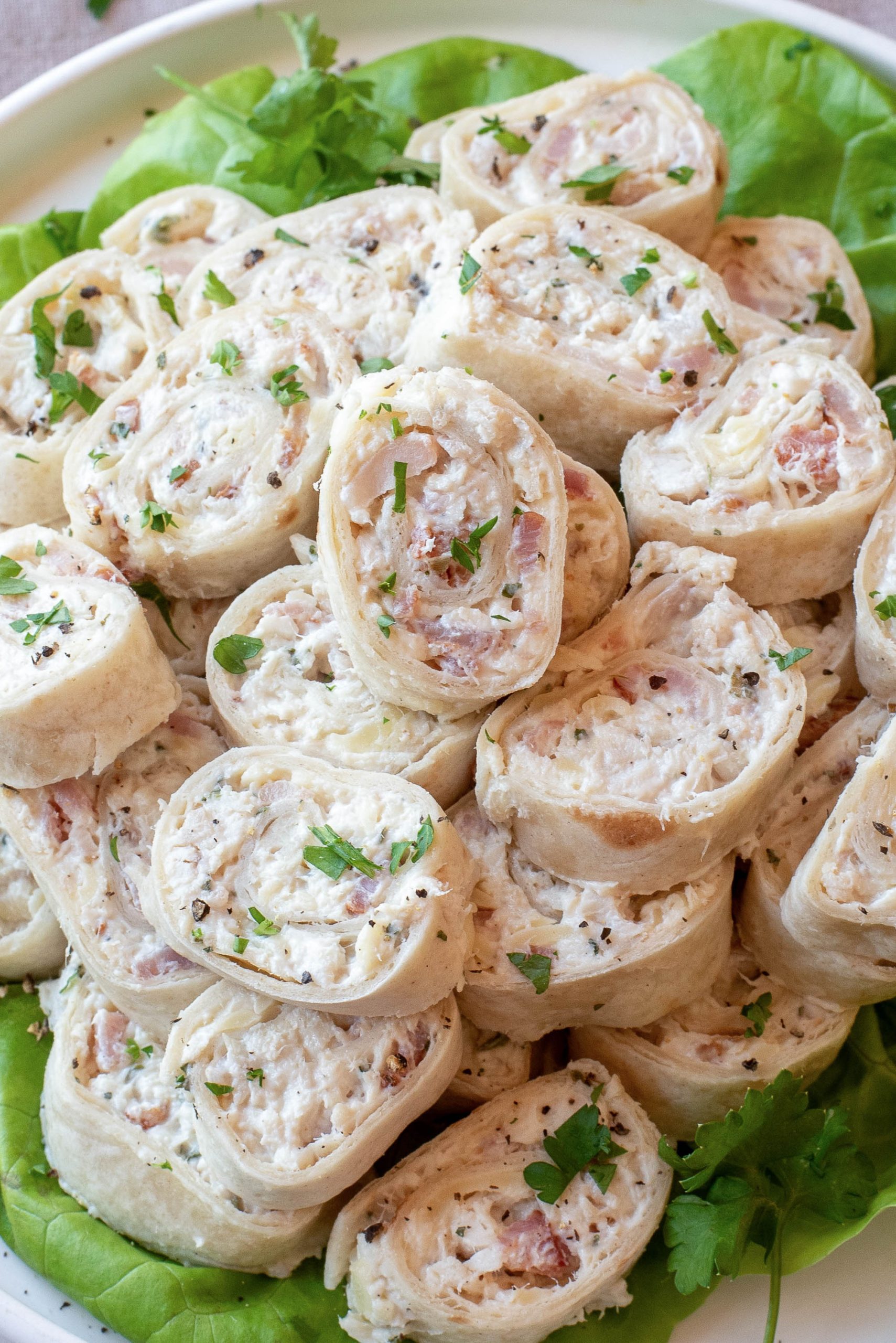 A platter of Chicken Bacon Ranch Pinwheels filled with a creamy mixture of meat and herbs, garnished with chopped parsley and served on a bed of lettuce.