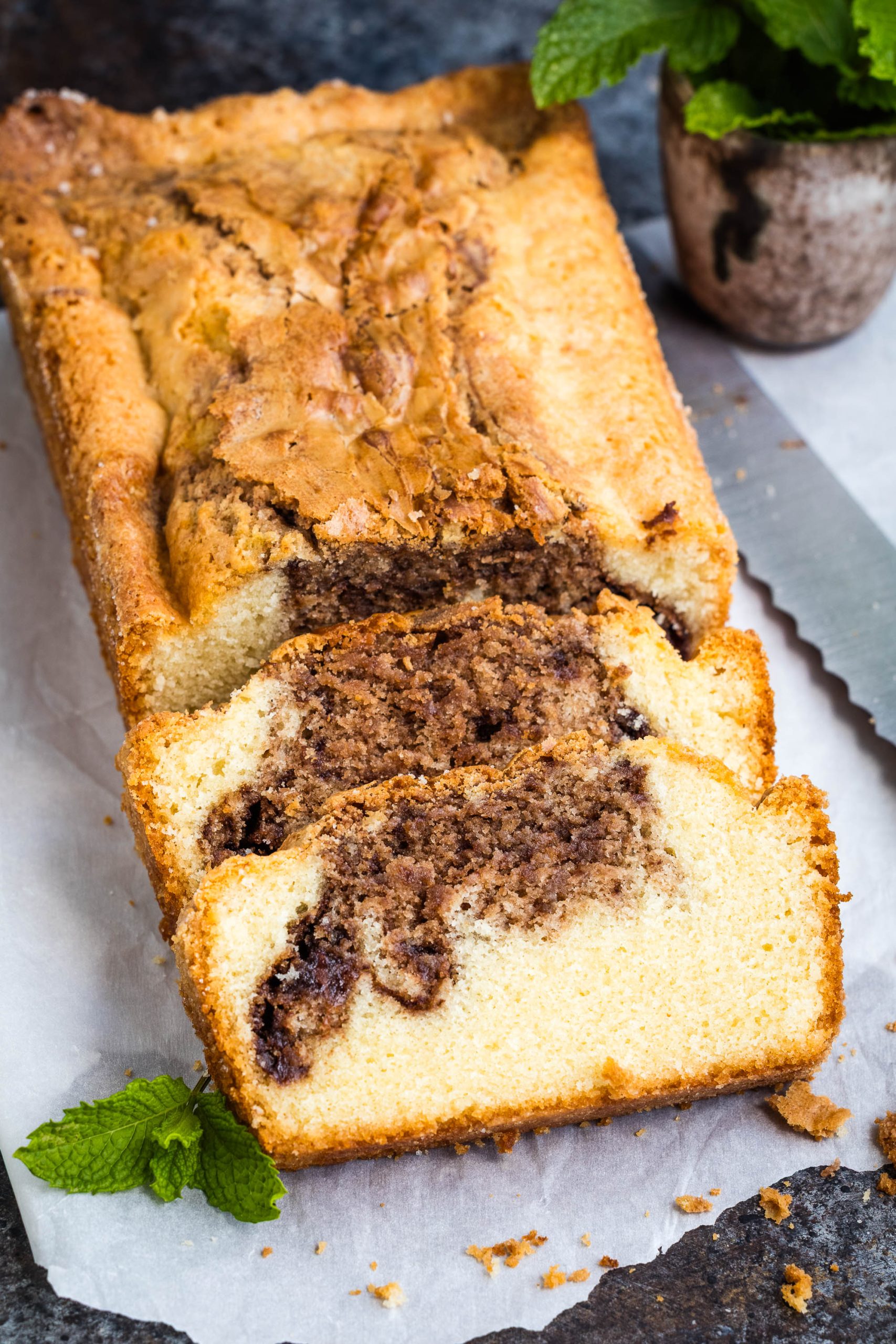 A sliced loaf of dessert with a swirl of chocolate and vanilla on a parchment-lined surface, garnished with a sprig of mint.