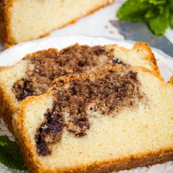 Two slices of Nutella Marble Pound Cake are served on a white plate, with a loaf and mint leaves in the background.