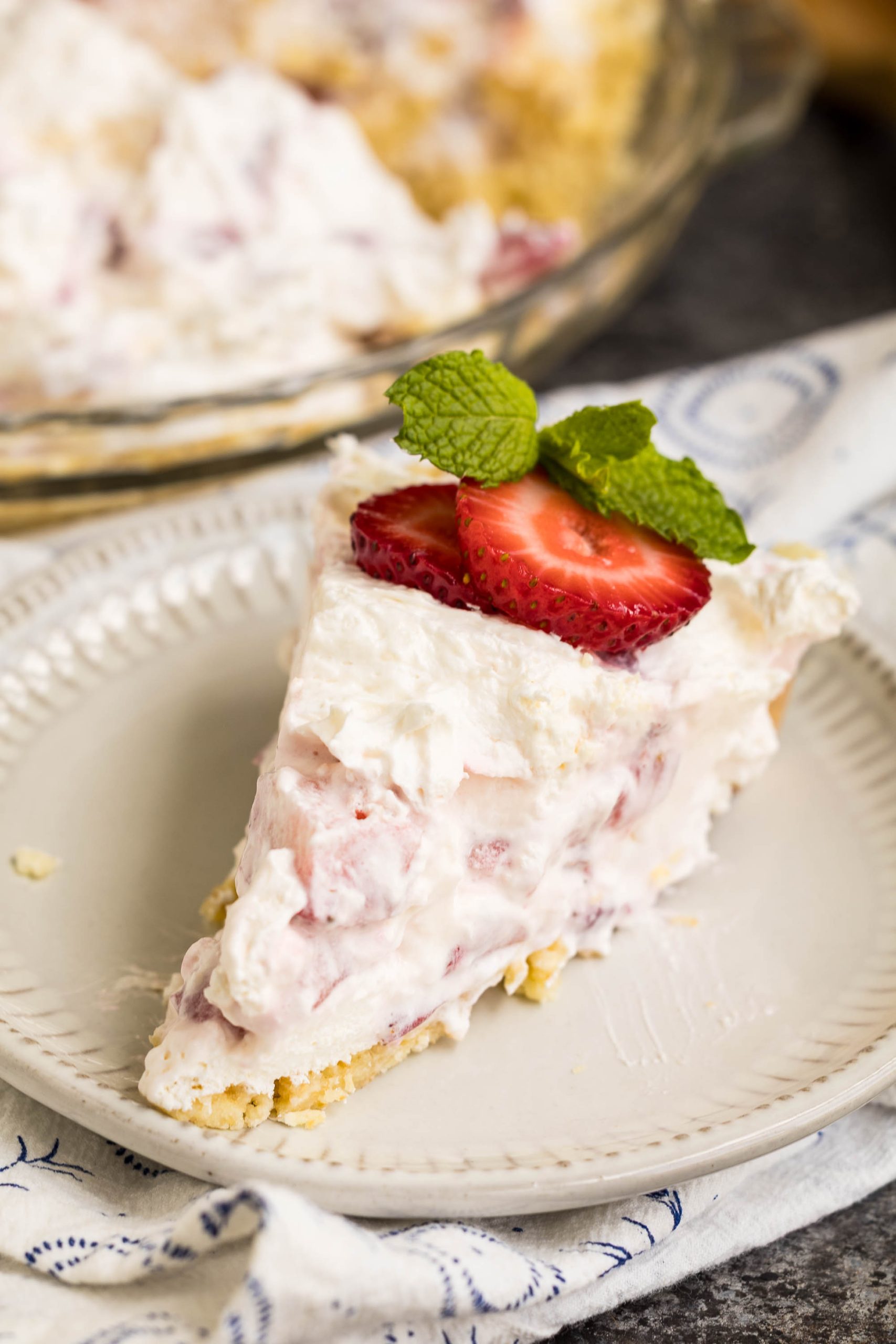 A slice of creamy strawberry pie topped with fresh strawberry slices and mint leaves on a white plate.