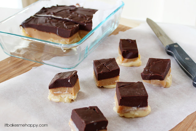 Glass baking dish with layered chocolate and caramel fudge, some pieces cut and placed on parchment paper next to a knife—a delicious treat inspired by 50 Shades of Chocolate.